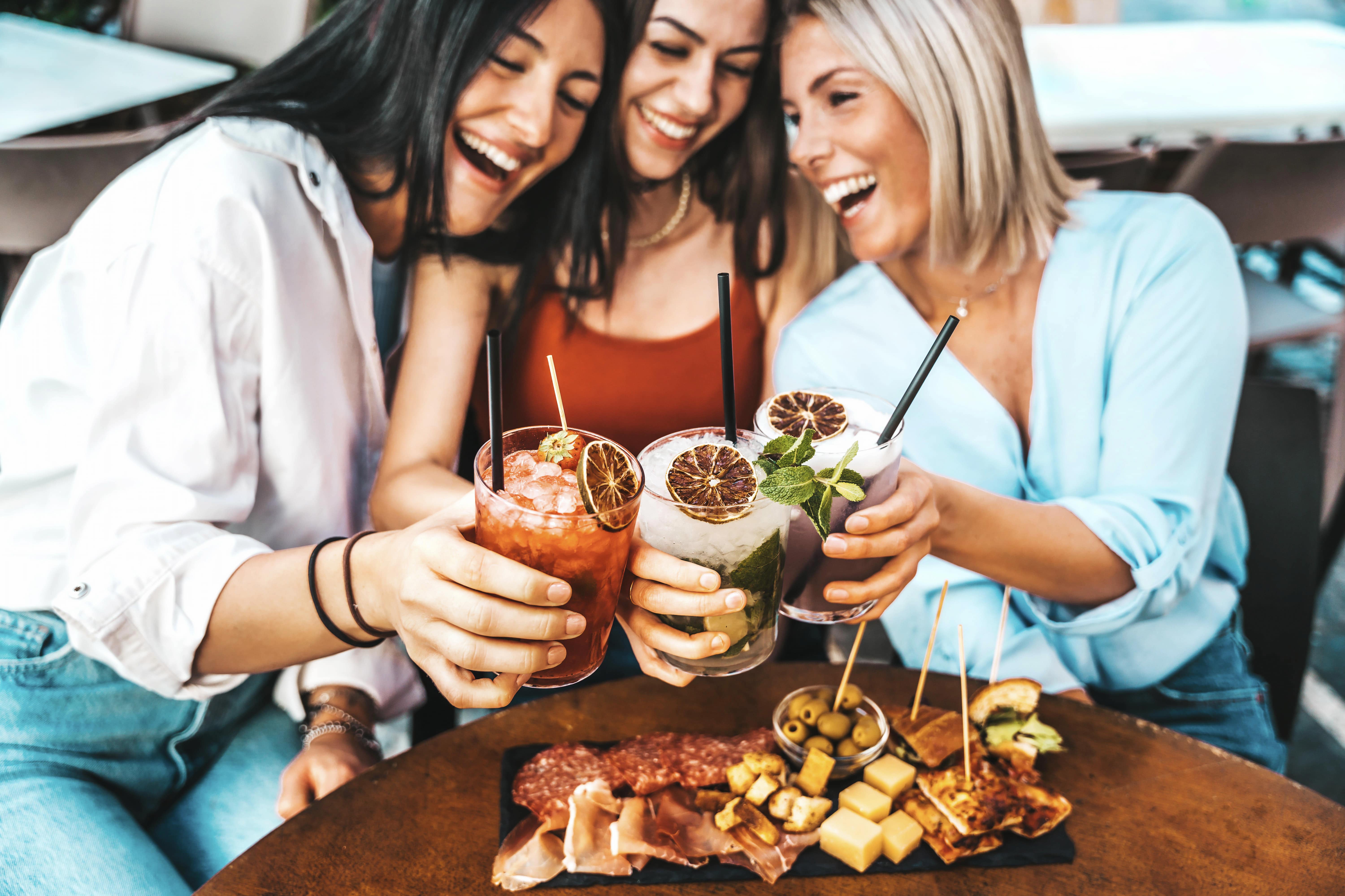 Three women enjoying cocktails and appetizers at a restaurant, smiling and raising their drinks. Water filters for restaurants ensure clean and safe water for preparing beverages and food, enhancing the overall dining experience.