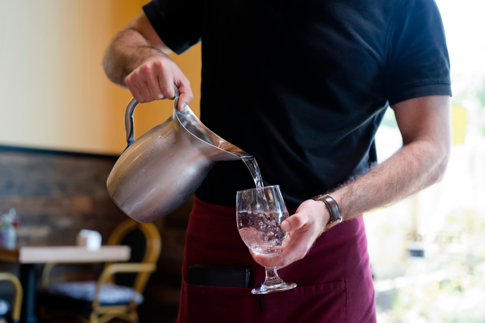 image of a waiter serving water from a steel jug