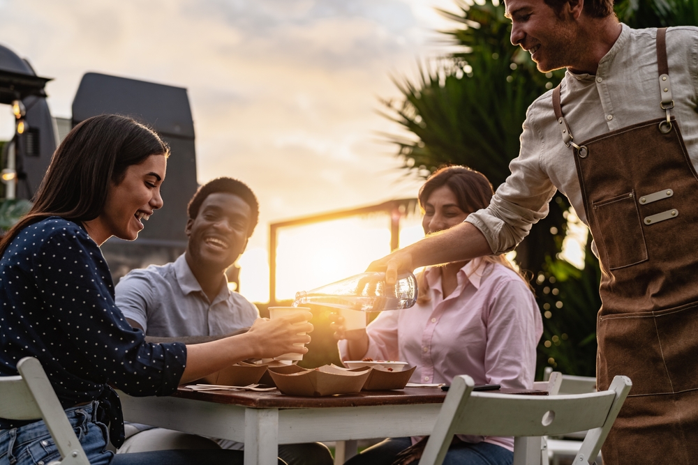 Happy multiracial people having fun eating while the waiter pouring some water.
