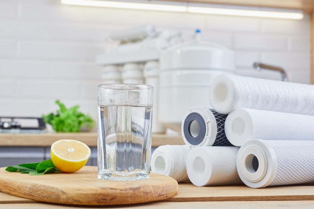 Glass of filtered clean water with reverse osmosis filter, lemons and cartridges on a table in kitchen.